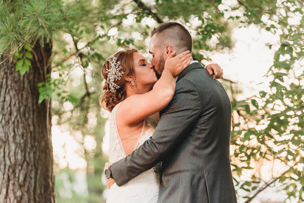 bride and groom kiss at sunset in front of trees at a woolery mill wedding