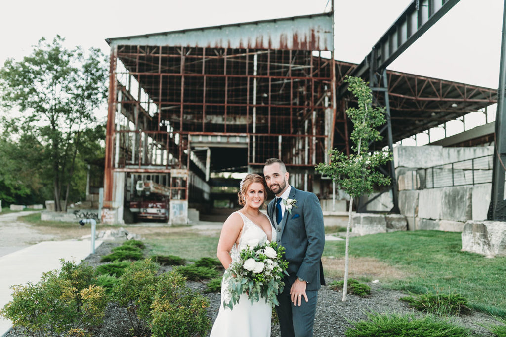 bride and groom smiling in front of the old woolery mill on their wedding day