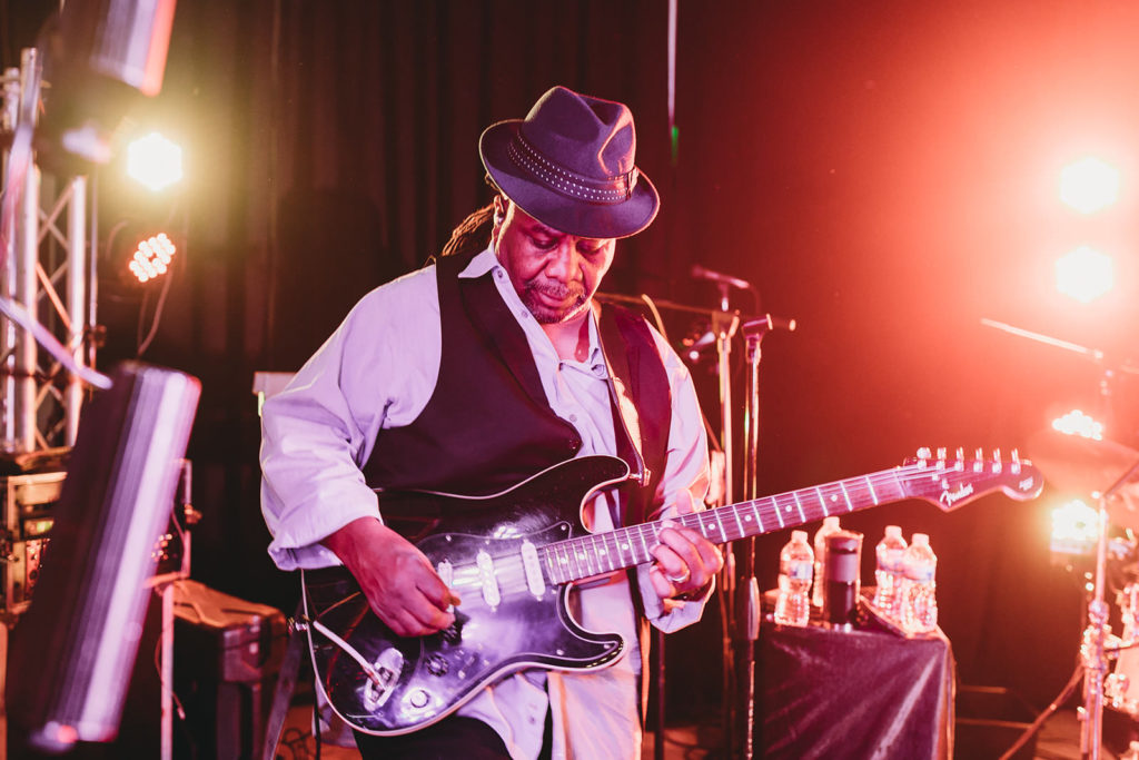 man in red light wearing fedora playing guitar at a woolery mill wedding