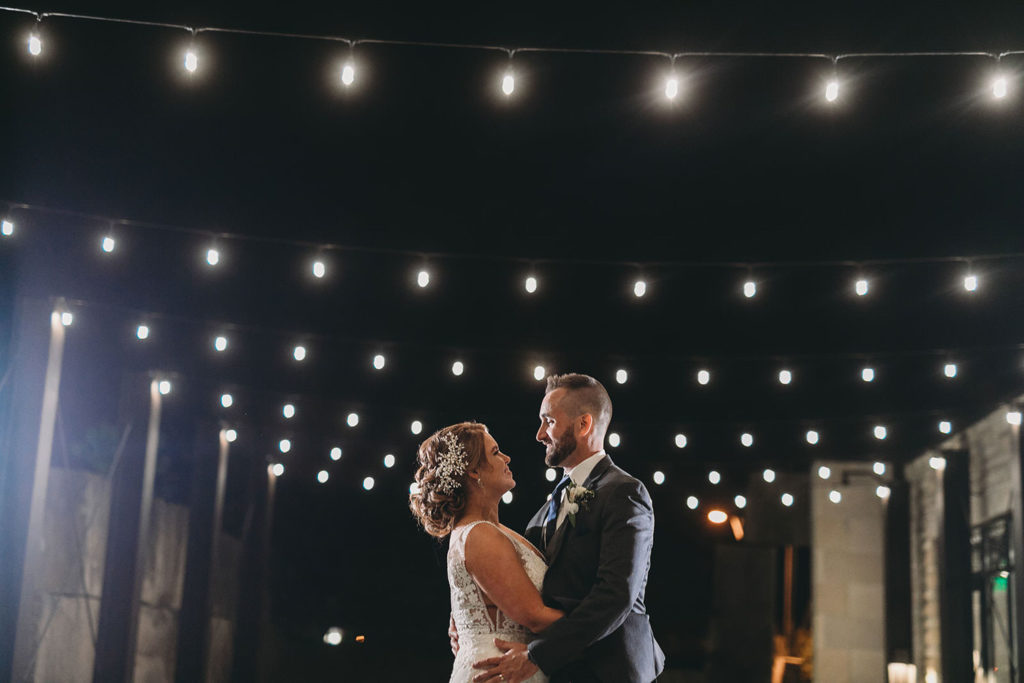bride and groom under string lights at night at a woolery mill wedding
