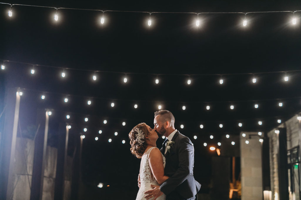 bride and groom kissing under string lights at night at a woolery mill wedding