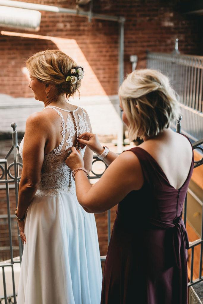 blonde woman buttons up bride's dress at mill top wedding noblesville