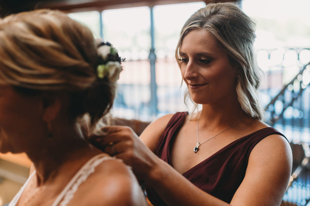 blonde woman helps bride into dress at mill top wedding noblesville
