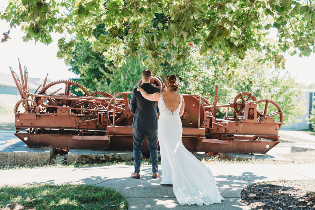 bride taps groom on shoulder in front of giant machinery at a woolery mill wedding