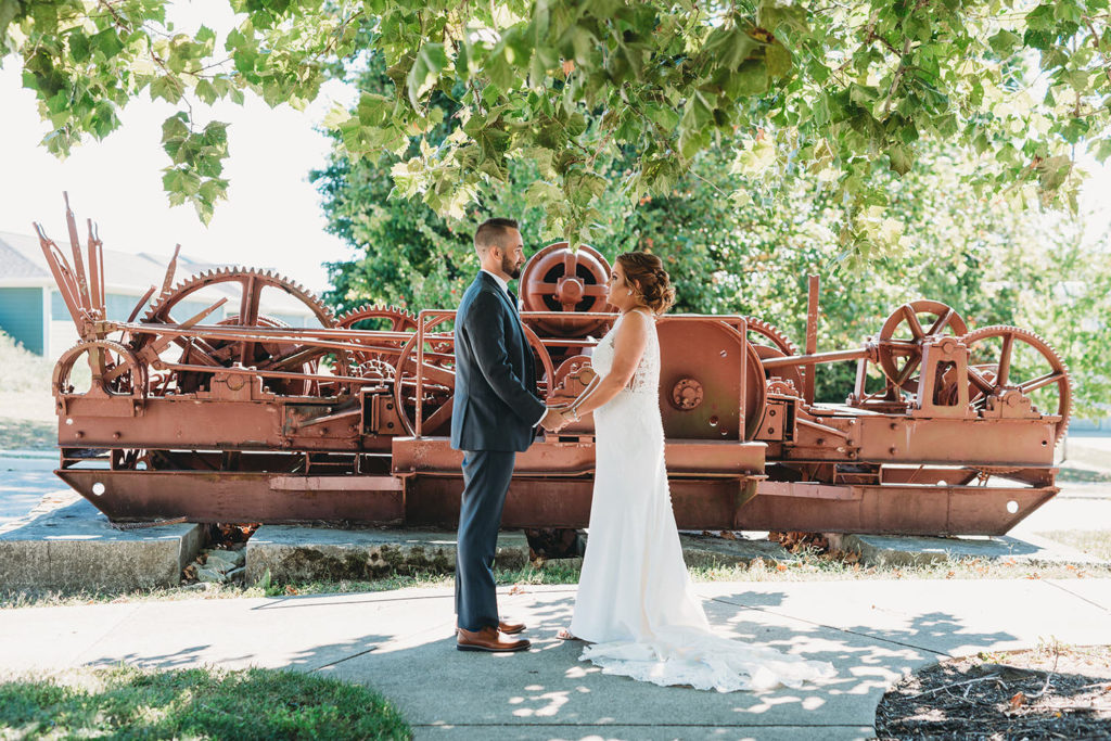 bride and groom hold hands in front of old machine at a woolery mill wedding