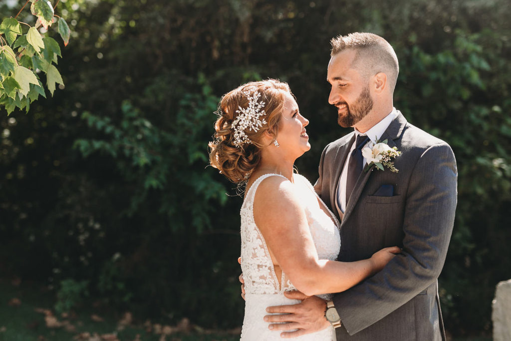 bride and groom hug in front of dark green leaves at a woolery mill wedding