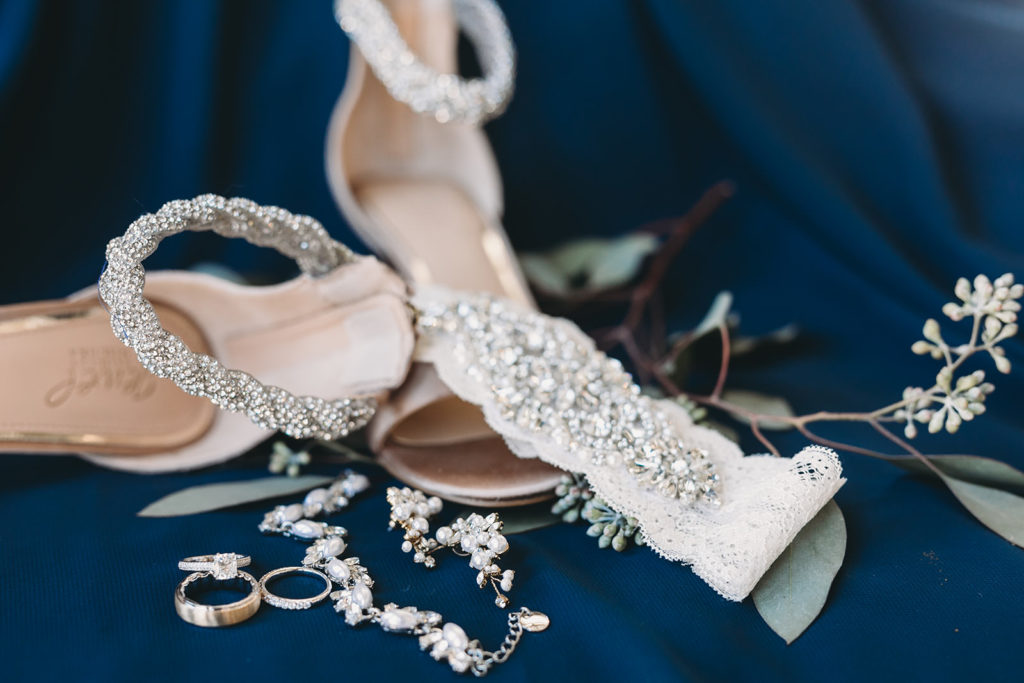 shoes, garters, rings, jewelry, and flowers on blue at a bloomington wedding