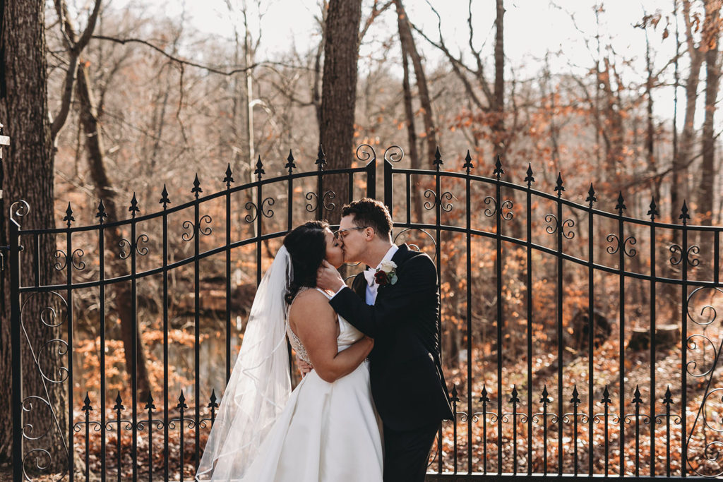 bride and groom kiss in front of gate in fall at bluffs wedding