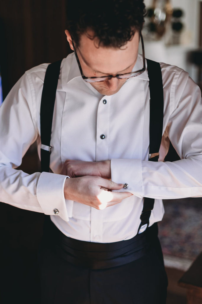 groom puts on cufflinks before bluffs wedding