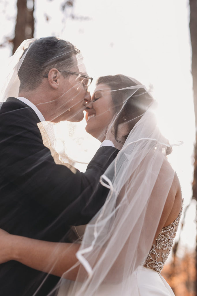 bride and groom kiss under veil at bluffs wedding