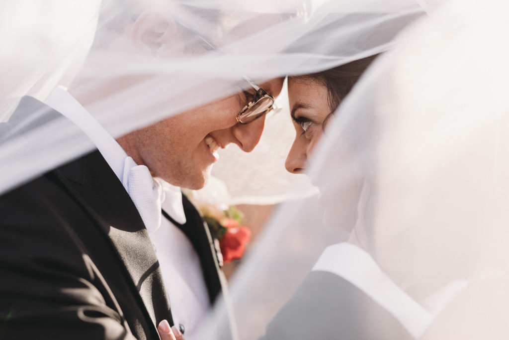 bride and groom smile under veil at bluffs wedding