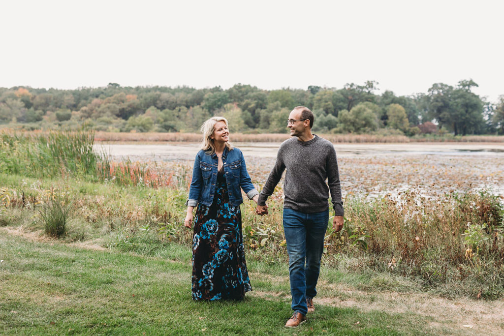man and woman hold hands and walk during their sand creek engagement