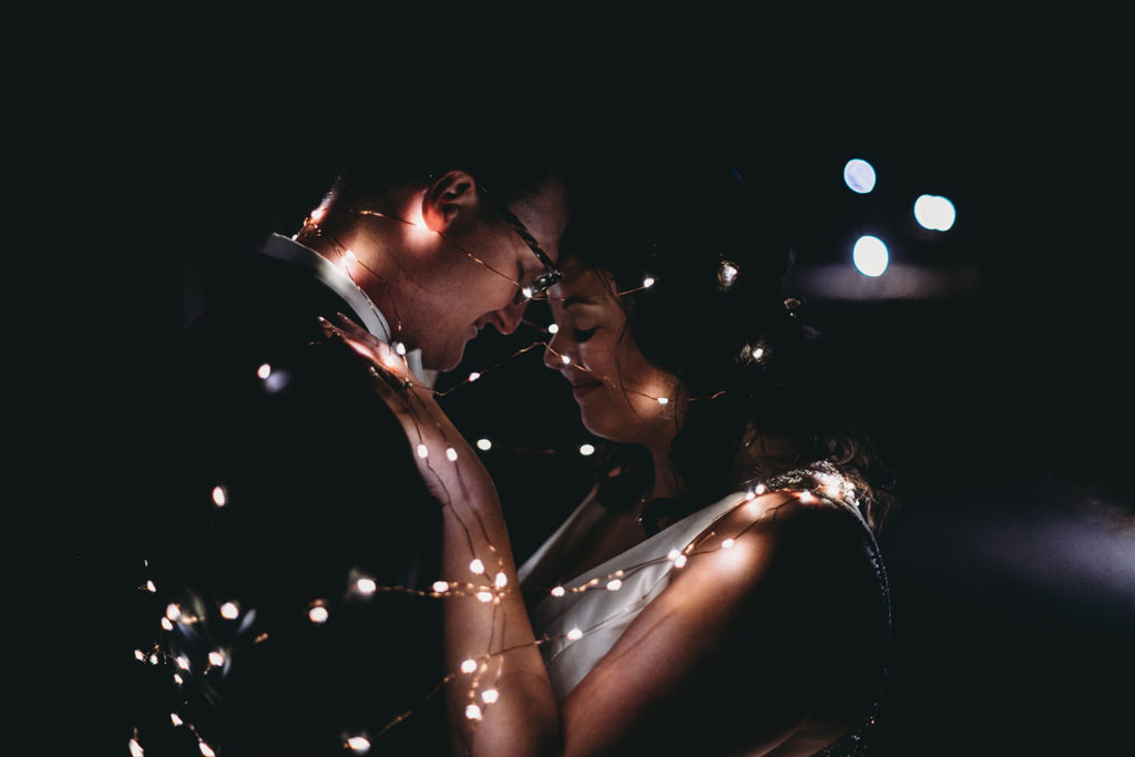 bride and groom wrapped up in fairy lights at night at bluffs wedding