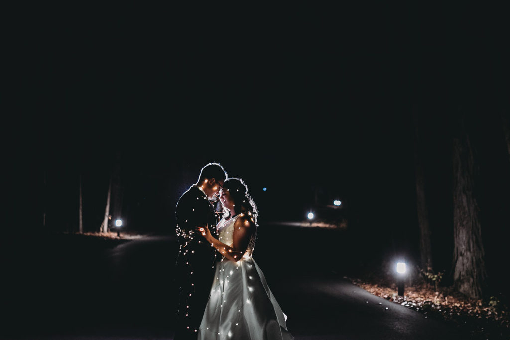 wide shot of bride and groom wrapped up in fairy lights at bluffs wedding