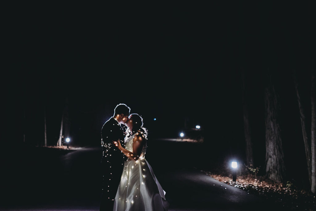 bride and groom kiss while wrapped in fairy lights at bluffs wedding