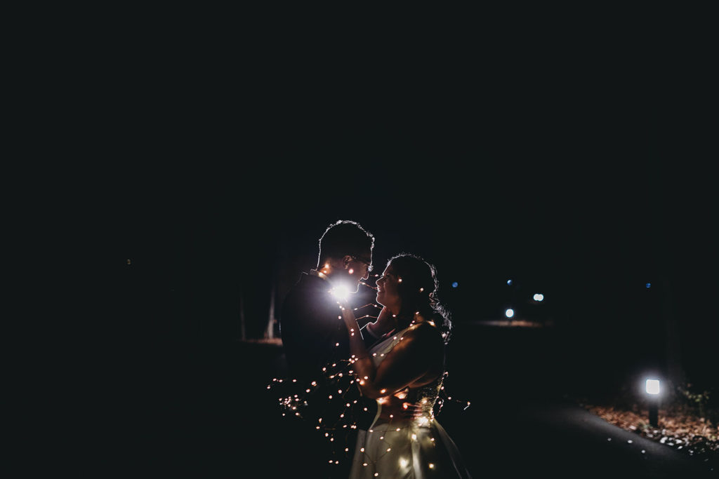 flash pop behind hugging bride and groom at night wrapped in string lights at bluffs wedding