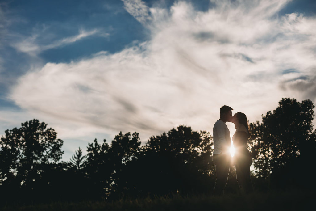 silhouette of man and woman kissing with sunstar in between them at their coxhall gardens engagement session