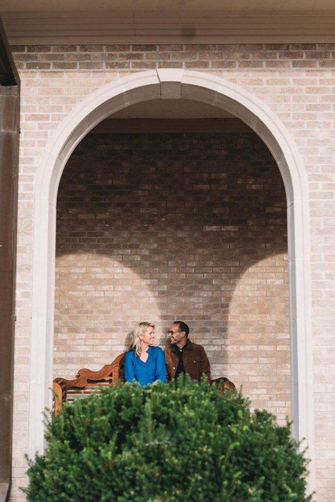 man and woman sit on bench under arch during their sand creek engagement