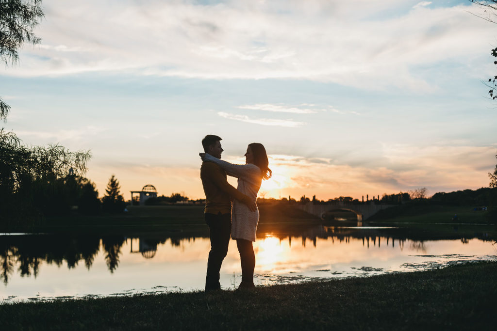 silhouette of man and woman hugging in front of pond at sunset at their coxhall gardens engagement session