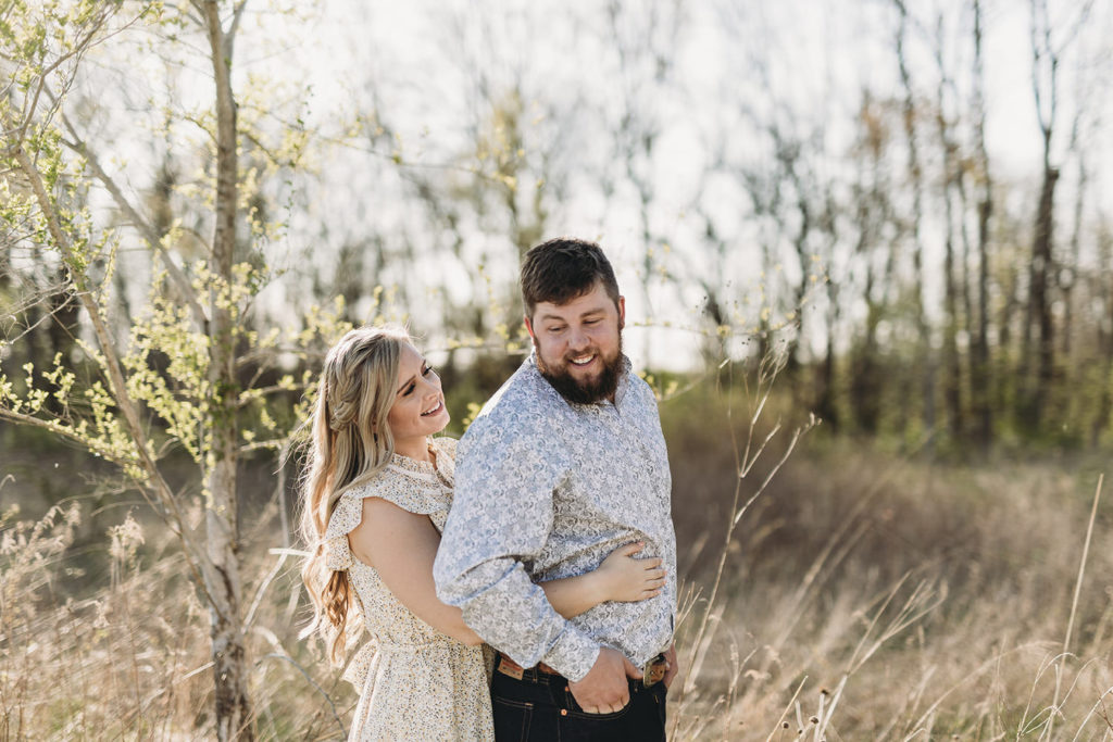 blond woman hugs man from behind during their Noblesville park engagement session