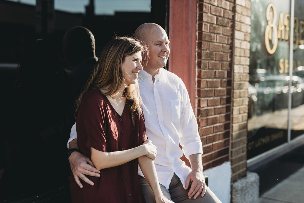 man and woman sit on window sill at sunset during their Fountain Square Engagement Photos