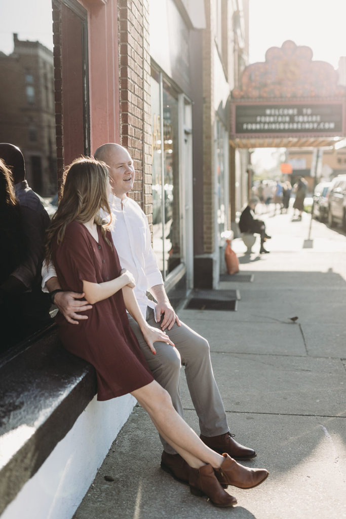 man and woman sit and laugh on edge of window sill during their Fountain Square Engagement Photos