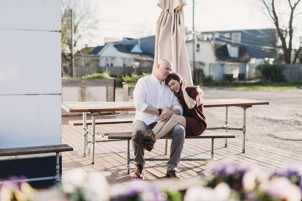 man and woman sit at table with umbrella and snuggle during their Fountain Square Engagement Photos