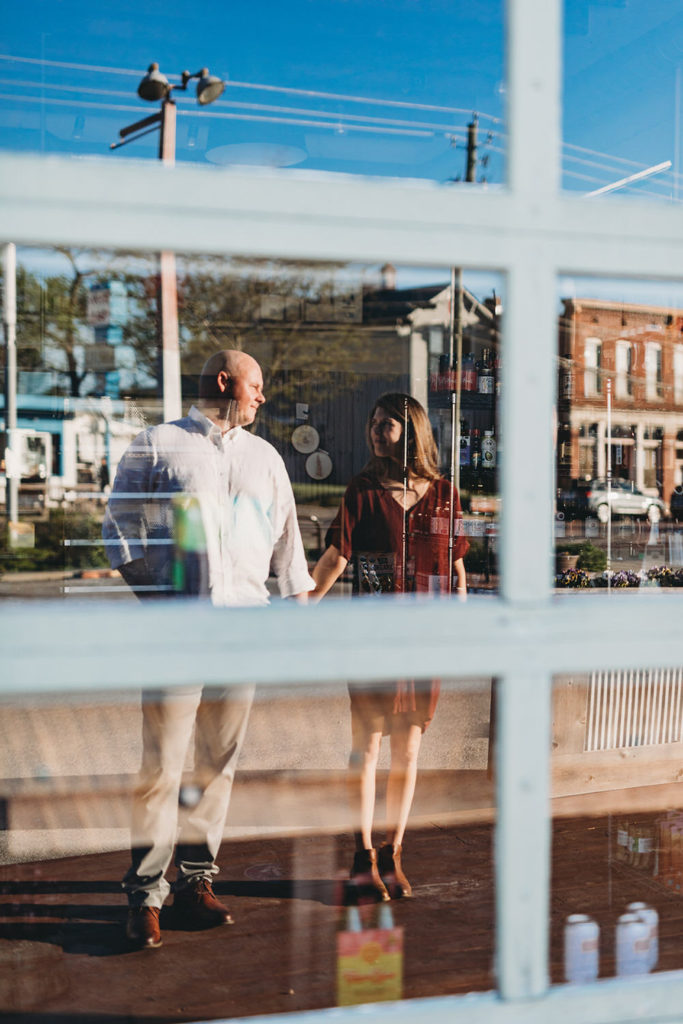 reflection of man and woman holding hands in glass window during their Fountain Square Engagement Photos