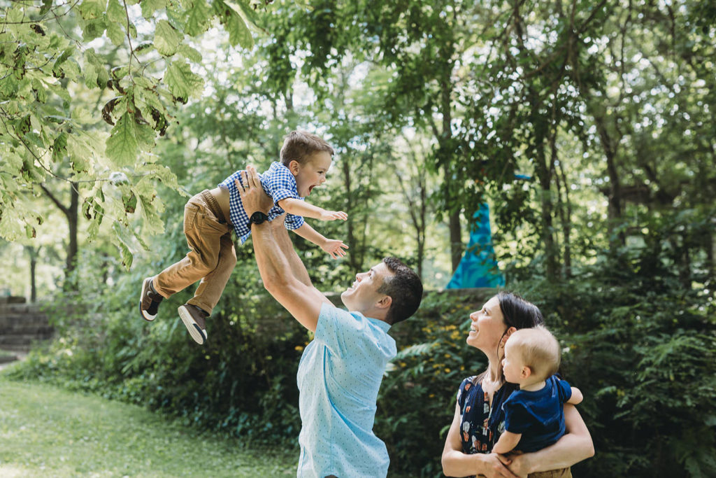 dad throws son in air while mom and other son watch at indianapolis art center ARTSPARK for broad ripple family photos
