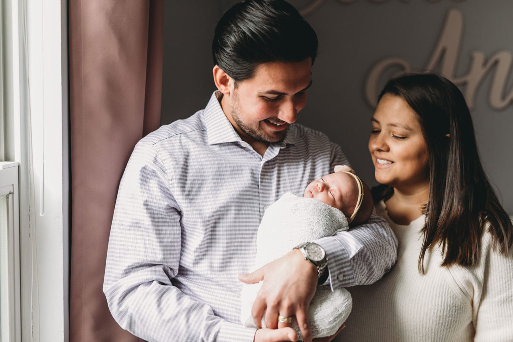 mom and dad hold baby next to window captured by their Indy Newborn Photographer