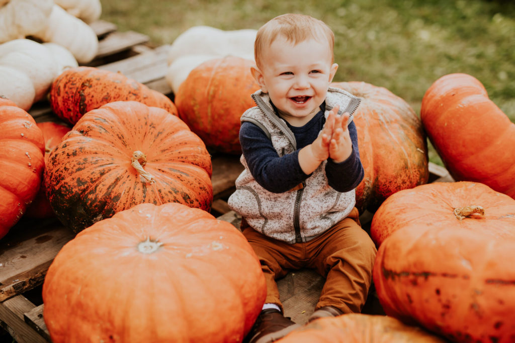 baby smiles, laughs, and claps in the middle of pumpkins during their Russell Farms Family Photos