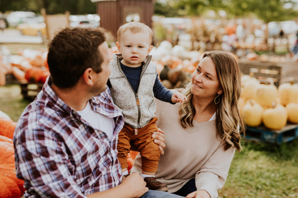 mom and dad hug child in pumpkin patch during their Russell Farms Family Photos