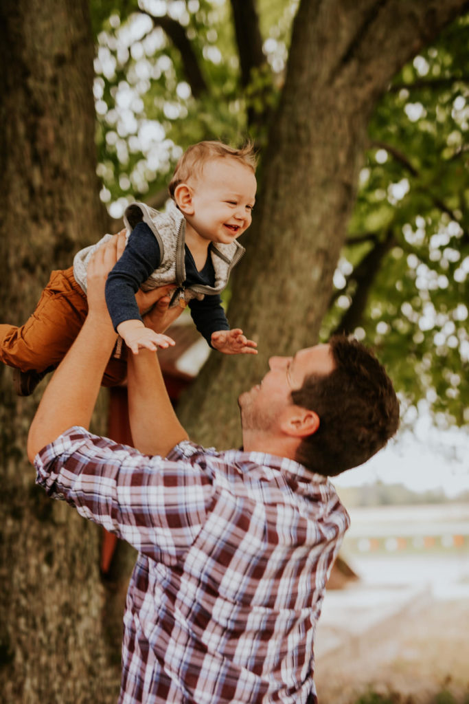 dad throws baby in air under a tree at a farm