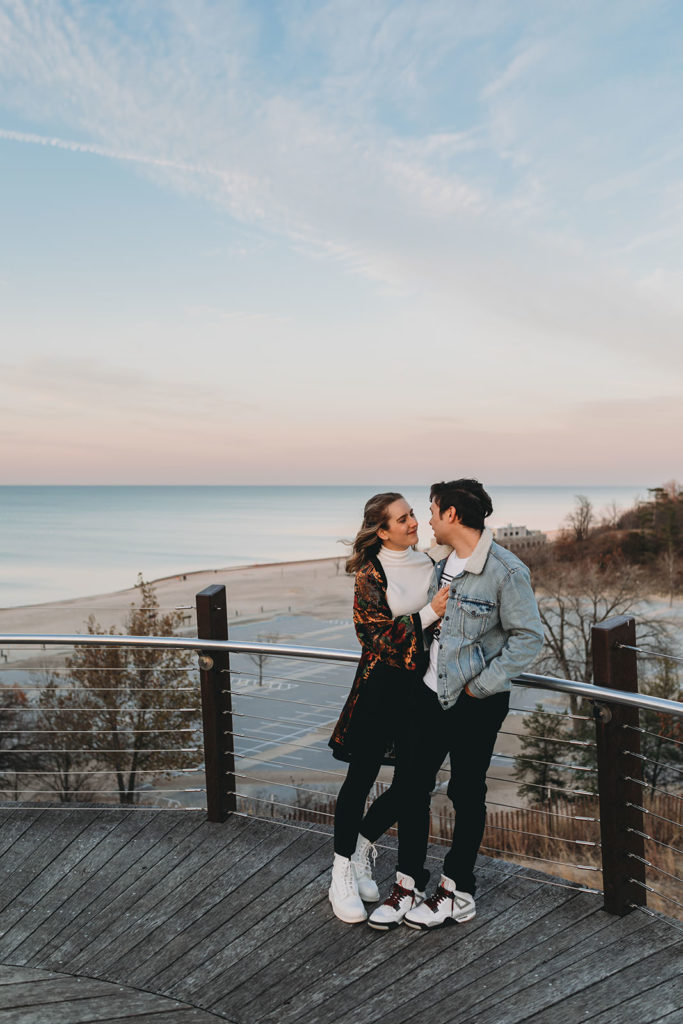 pink hues in the sky while young couple looks at each other during their Indiana Dunes engagement photos