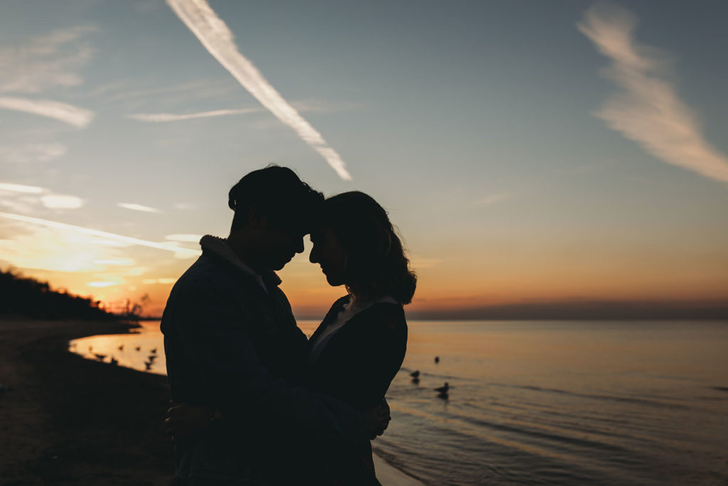 young couple touches foreheads on the shore of lake michigan during their Indiana Dunes engagement photos