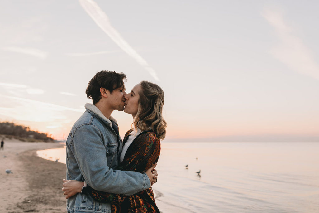 young couple kiss on shore of lake michigan during their Indiana Dunes engagement photos