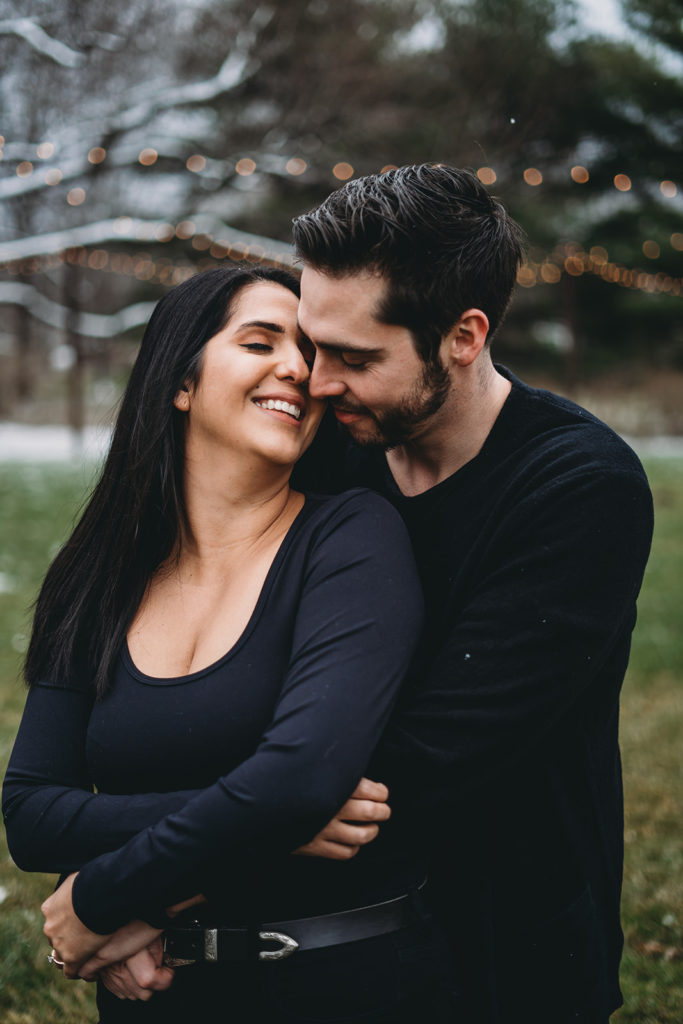 man hugs woman from behind and she leans back to kiss his during their mustard seed gardens engagement photos