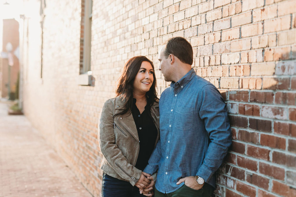 man and woman talk while leaning against a brick wall at sunset during their downtown zionsville engagement session