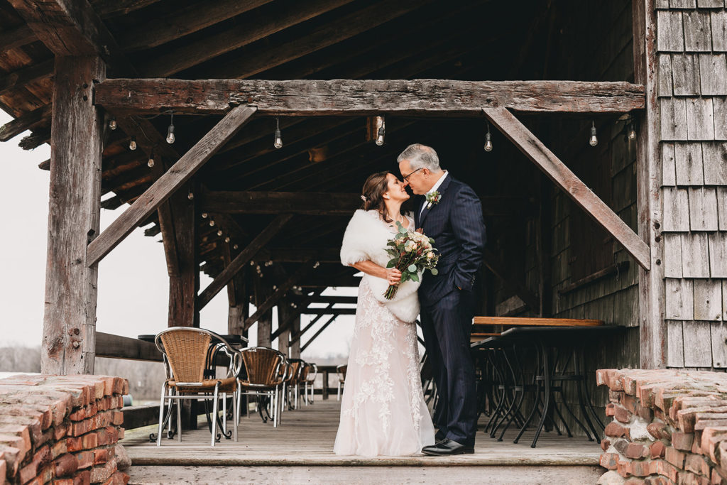 bride and groom in winter clothes kiss under frame of building during their traders point creamery elopement