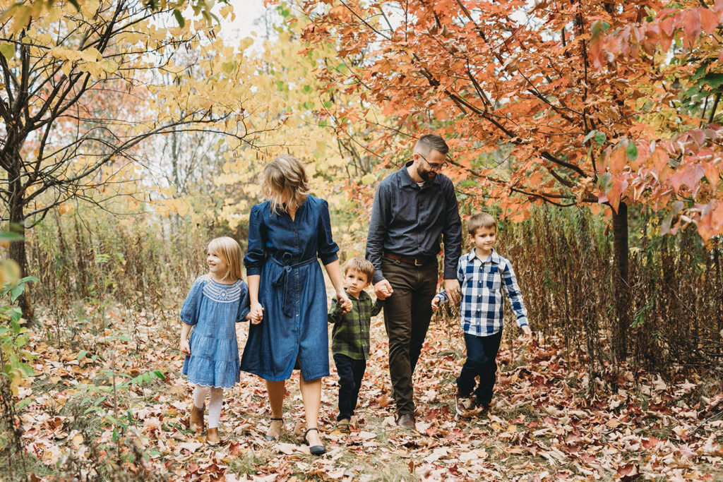 family of five walking through fall colors in forest captured by a Carmel Family Photographer
