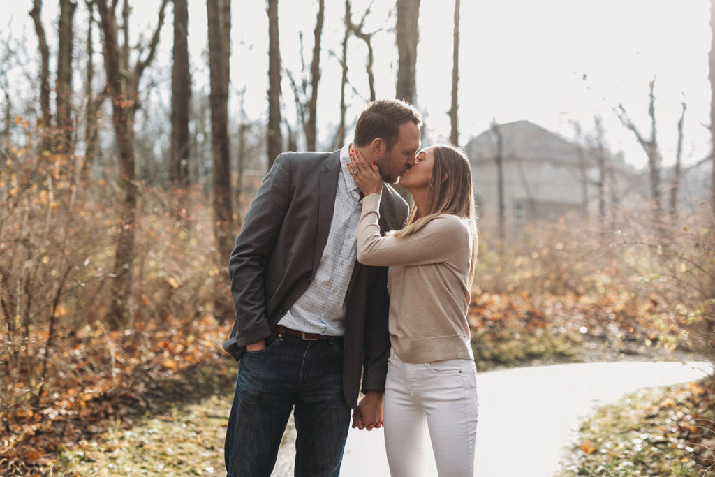 young engaged couple kiss in woods captured by their Noblesville Photographer