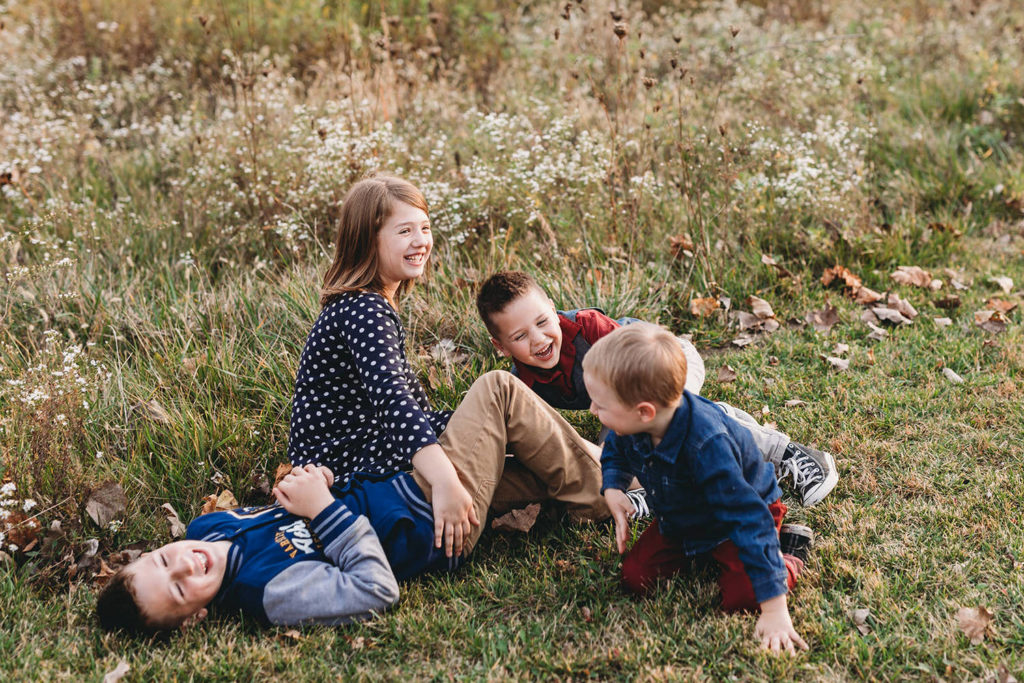 four kids roll in the grass and laugh in these Carmel Fall Family Photos
