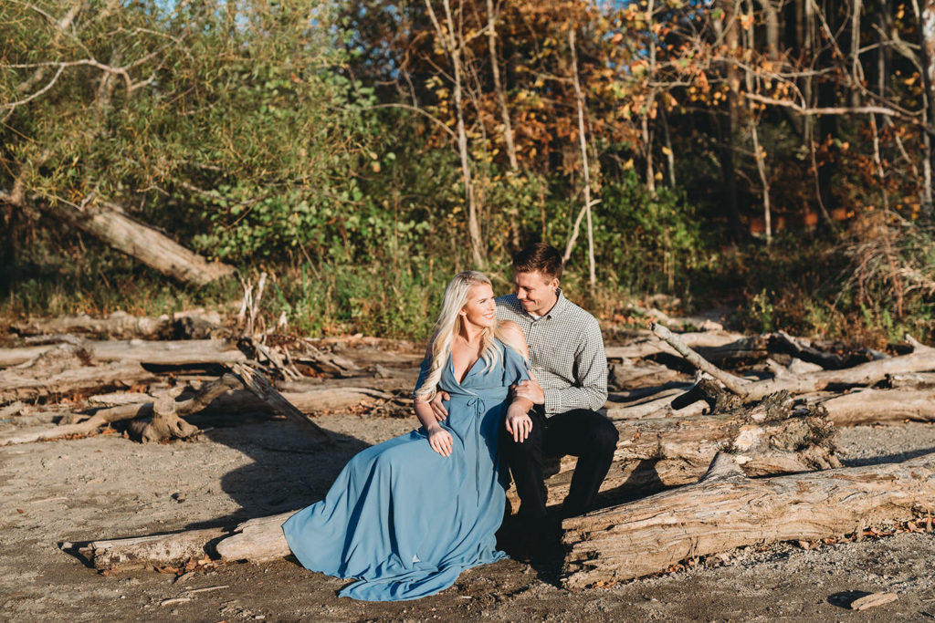 blonde woman and man sit on logs and look into each other's eyes during their eagle creek photo session