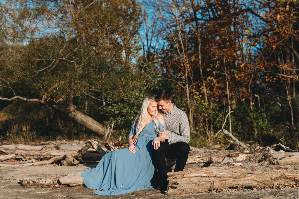 blonde woman in blue dress sits with man on driftwood in this eagle creek photo session
