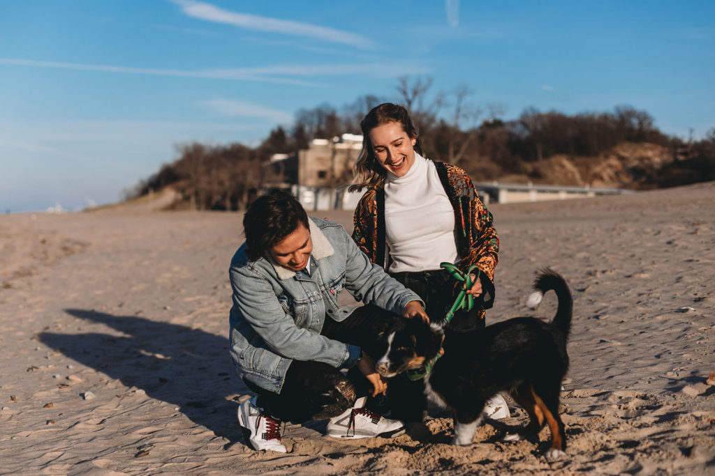 young couple pet their dog at the beach at lake michigan