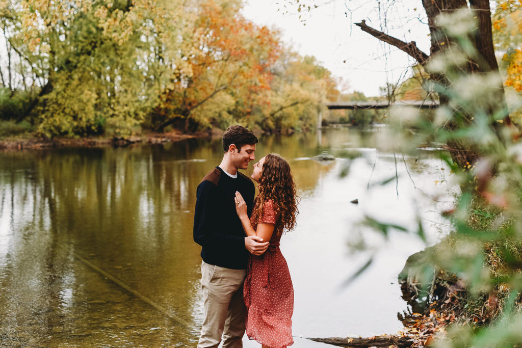 couple hug next to White River in Noblesville during their Potters Bridge Engagement session
