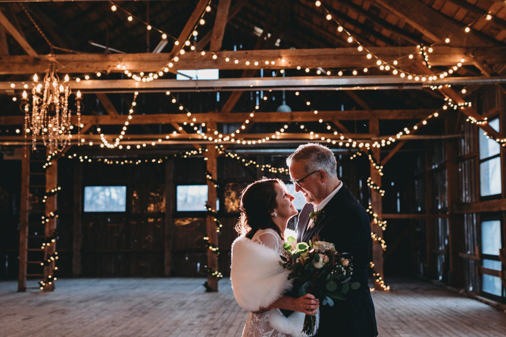 backlit by flash a bride and groom hug in a barn with fairy lights during their traders point creamery elopement