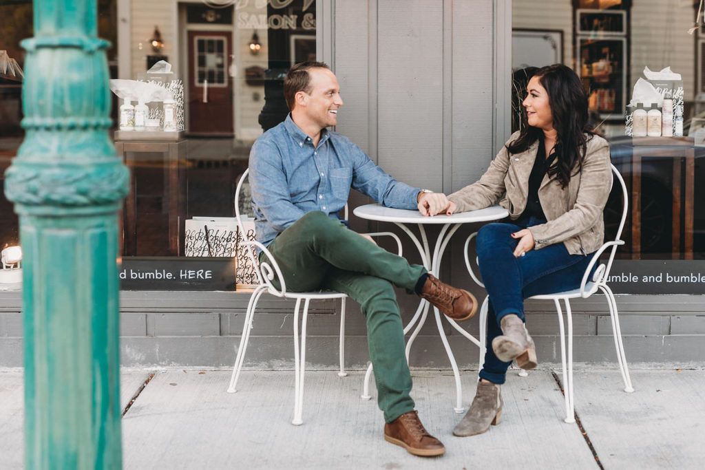 man and woman sit at table of little coffee shop during their downtown zionsville engagement session
