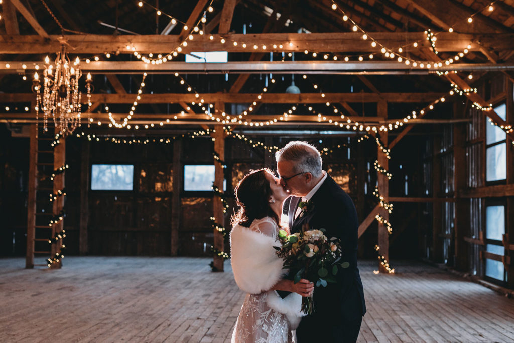 couple kisses in barn with lots of string lights during their traders point creamery elopement