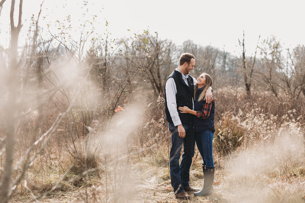 young engaged couple in field with tall grass captured by their Noblesville Photographer